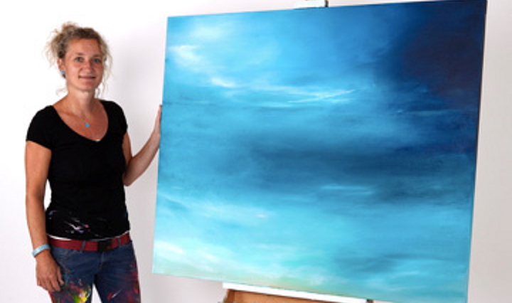 Peggy Schumacher neben einem großen Gemälde mit in einander fließenden Blautönen
