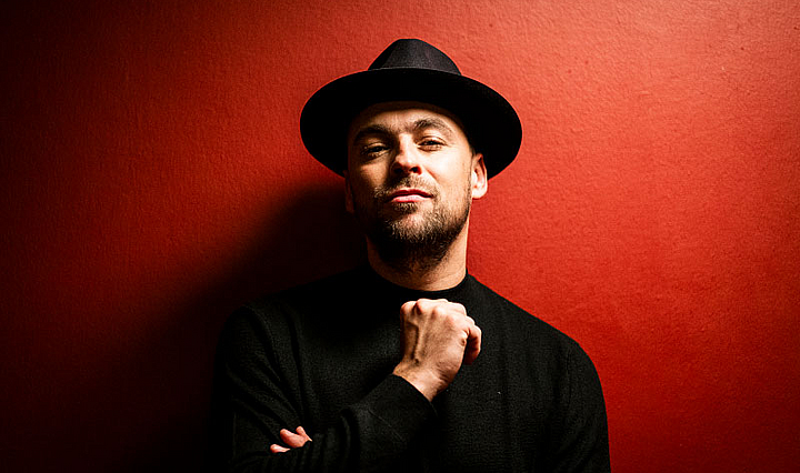 Der Sänger Max Mutzke mit Hut vor einer roten Wand