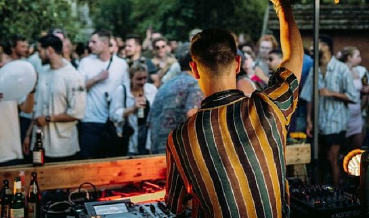 DJ hinter Pult mit Tanzender Menge im Freien